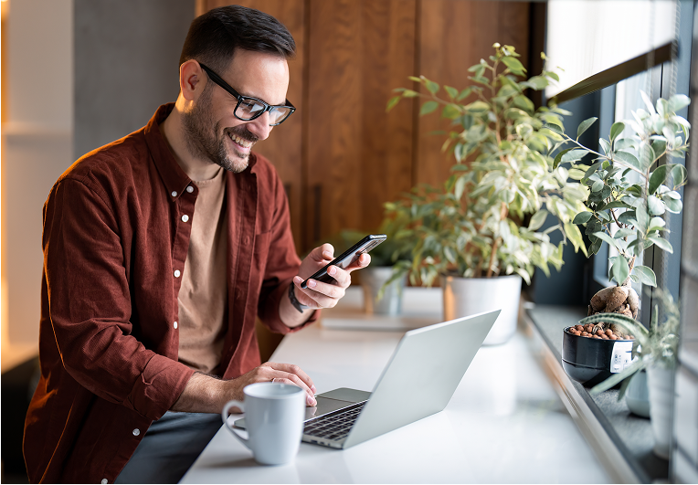Man using phone and laptop at desk.
