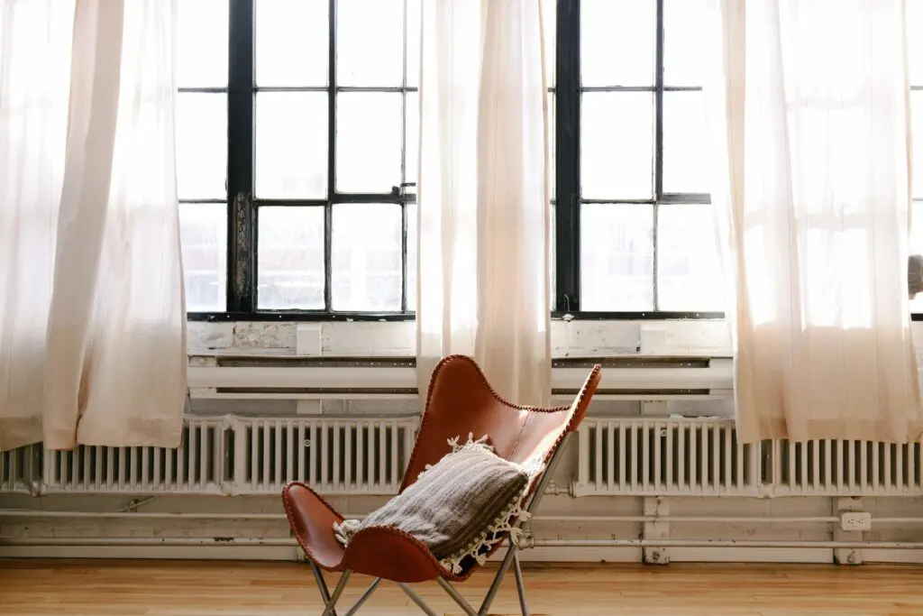 Chair by large windows with sheer curtains.